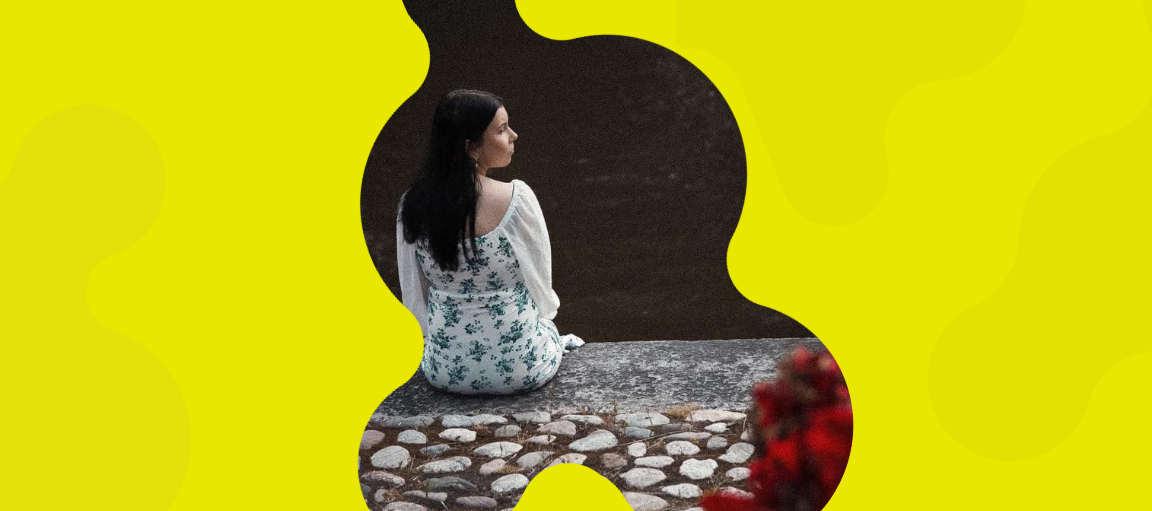 Nina istuu joenpenkalla selin kameraan.