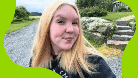 Vaaleahiuksinen nainen hymyilee ulkona.