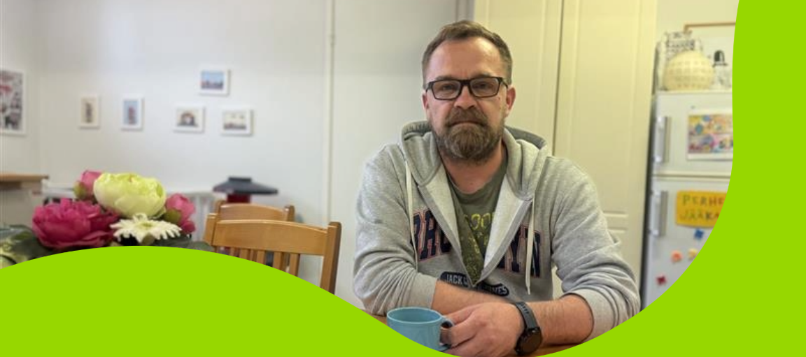 Mies istuu pöydän ääressä kahvikuppi kädessään.