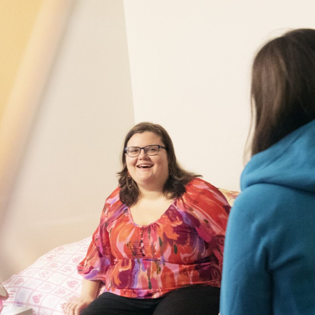 Sängyllä istuva nainen hymyilee.