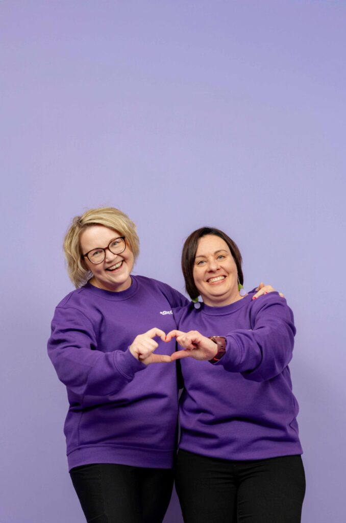 Kaksi hymyilevää Tavanan työntekijää mudostavat käsillään sydämen.