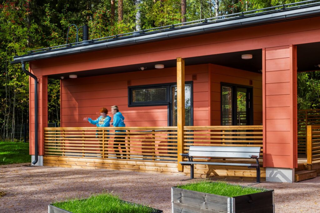 Punainen hirsirakennus, jonka terassilla kaksi hahmoa.
